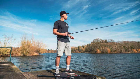 Hombre pescando en un lago, usando pantalón desmontable de la marca Fox Rage, paisaje natural de fondo.